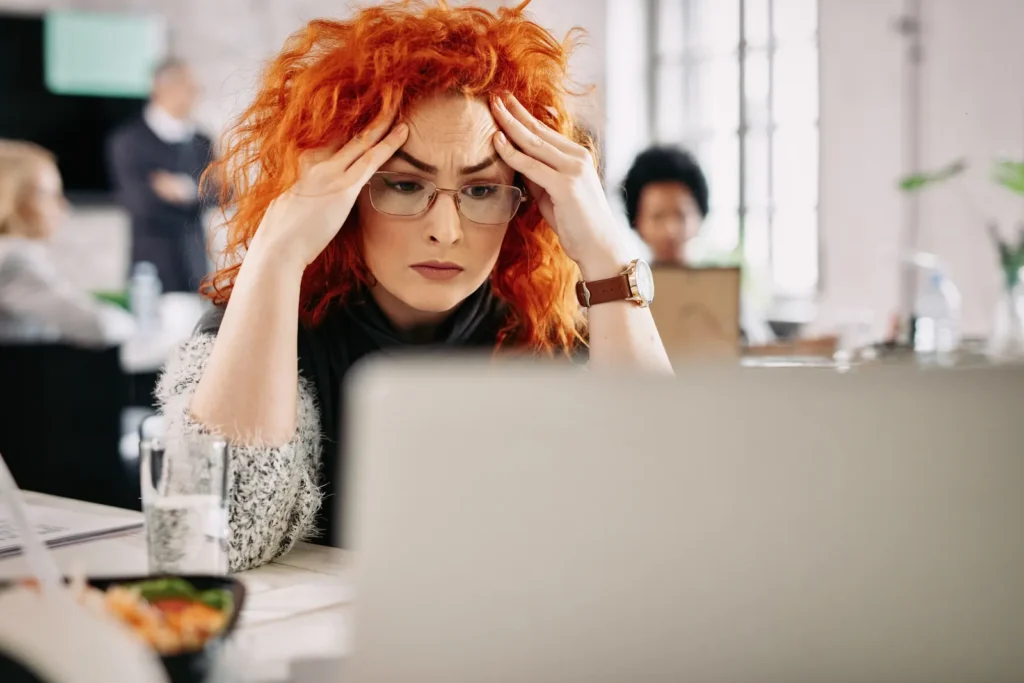 Impiegata preoccupata con le mani tra i capelli legge un messaggio di errore sul portatile in ufficio