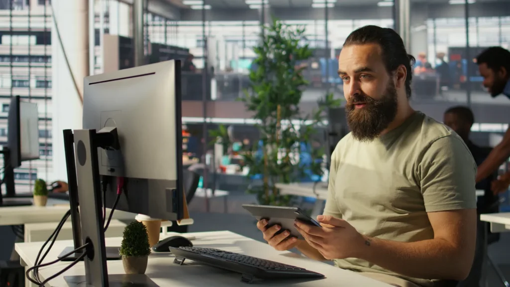 Impiegato in un piccolo ufficio controlla dati sul monitor con una tazza di caffè in mano